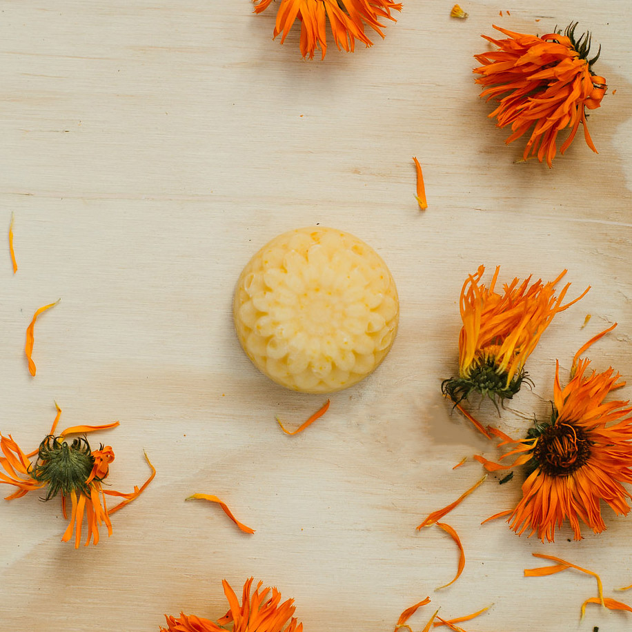 Image of a Busy Bee Soap - a creamy coloured soap moulded to look like honeycomb. Soap on a light wood table surrounded by calendular flowers and petals.