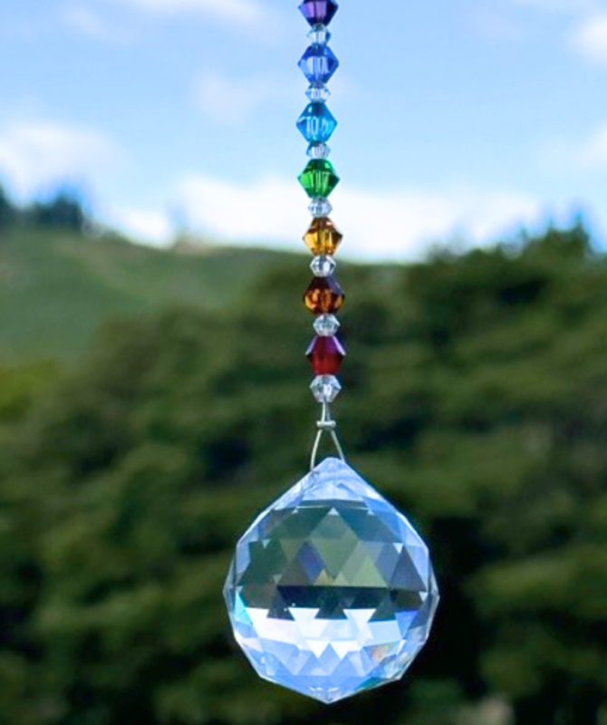 Crystal Chakra Sun Catcher shown against a blurred background of a greenery