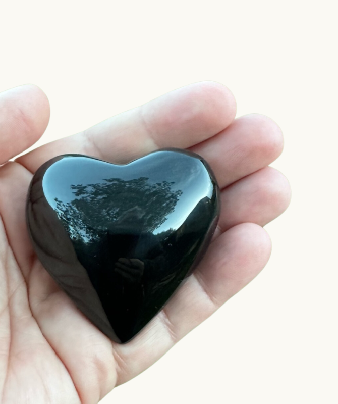 Black Obsidian Heart Being Held In The Palm Of A Hand On A White Background
